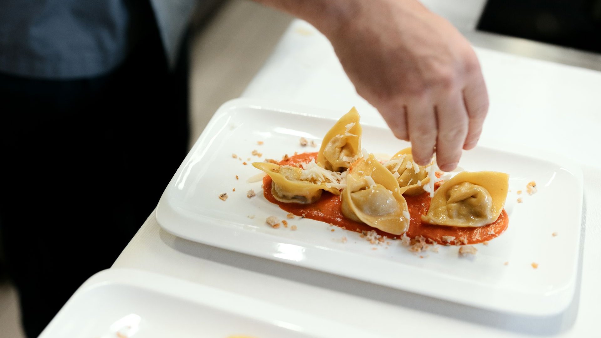 Il nostro hotel a 3 stelle in Val Gardena e la sua cucina Mano cosparge formaggio su tortellini con salsa di pomodoro su piatto bianco