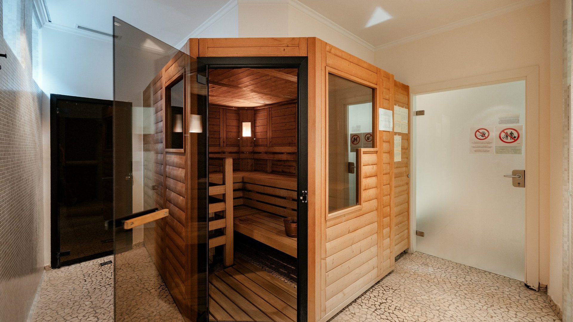 Hotel a Santa Cristina in Val Gardena con piscina: relax puro Stanza sauna moderna con porta in vetro aperta e panche in legno all'interno