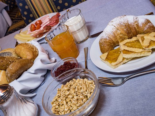 Il nostro hotel a 3 stelle in Val Gardena e la sua cucina Tavola per colazione con panini, croissant, affettati, cereali, succo e latte