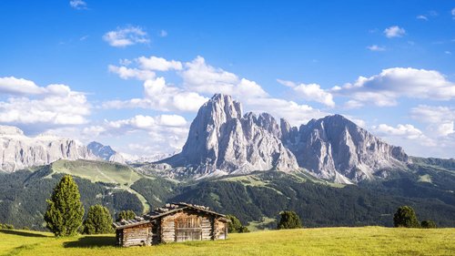 Hotel a 3 stelle a Santa Cristina: per un benessere stellare Capanna di legno su prato verde con montagne sullo sfondo e cielo azzurro