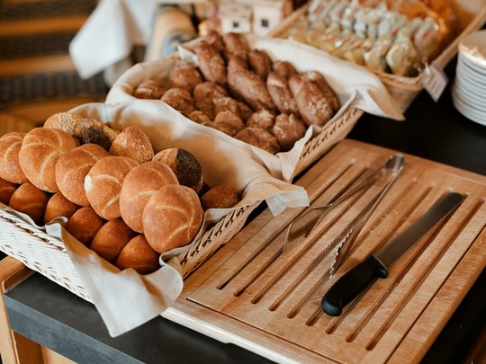 Il nostro hotel a 3 stelle in Val Gardena e la sua cucina Vari tipi di pane fresco in un cesto con coltello da pane e pinze su tagliere