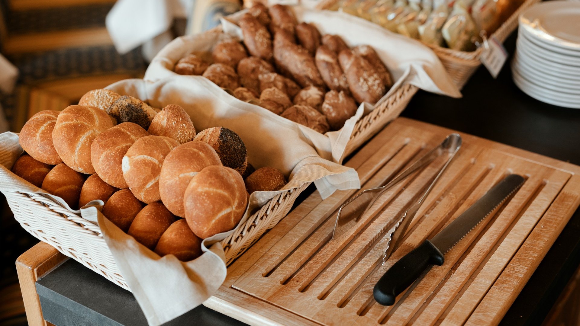 Il nostro hotel a 3 stelle in Val Gardena e la sua cucina Vari tipi di pane fresco in un cesto con coltello da pane e pinze su tagliere