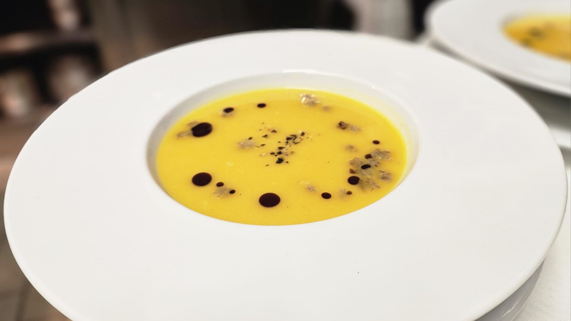 Il nostro hotel a 3 stelle in Val Gardena e la sua cucina Zuppa di zucca in piatto bianco con gocce decorative e spezie