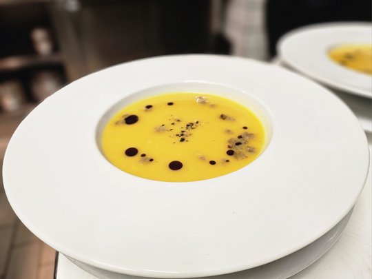 Il nostro hotel a 3 stelle in Val Gardena e la sua cucina Zuppa di zucca in piatto bianco con gocce decorative e spezie