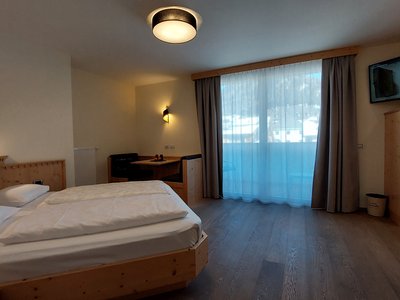 Deine Unterkunft in St. Christina im Grödnertal: Willkommen! Gemütliches Hotelzimmer mit Doppelbett, Sitzbereich und Balkon mit Vorhängen