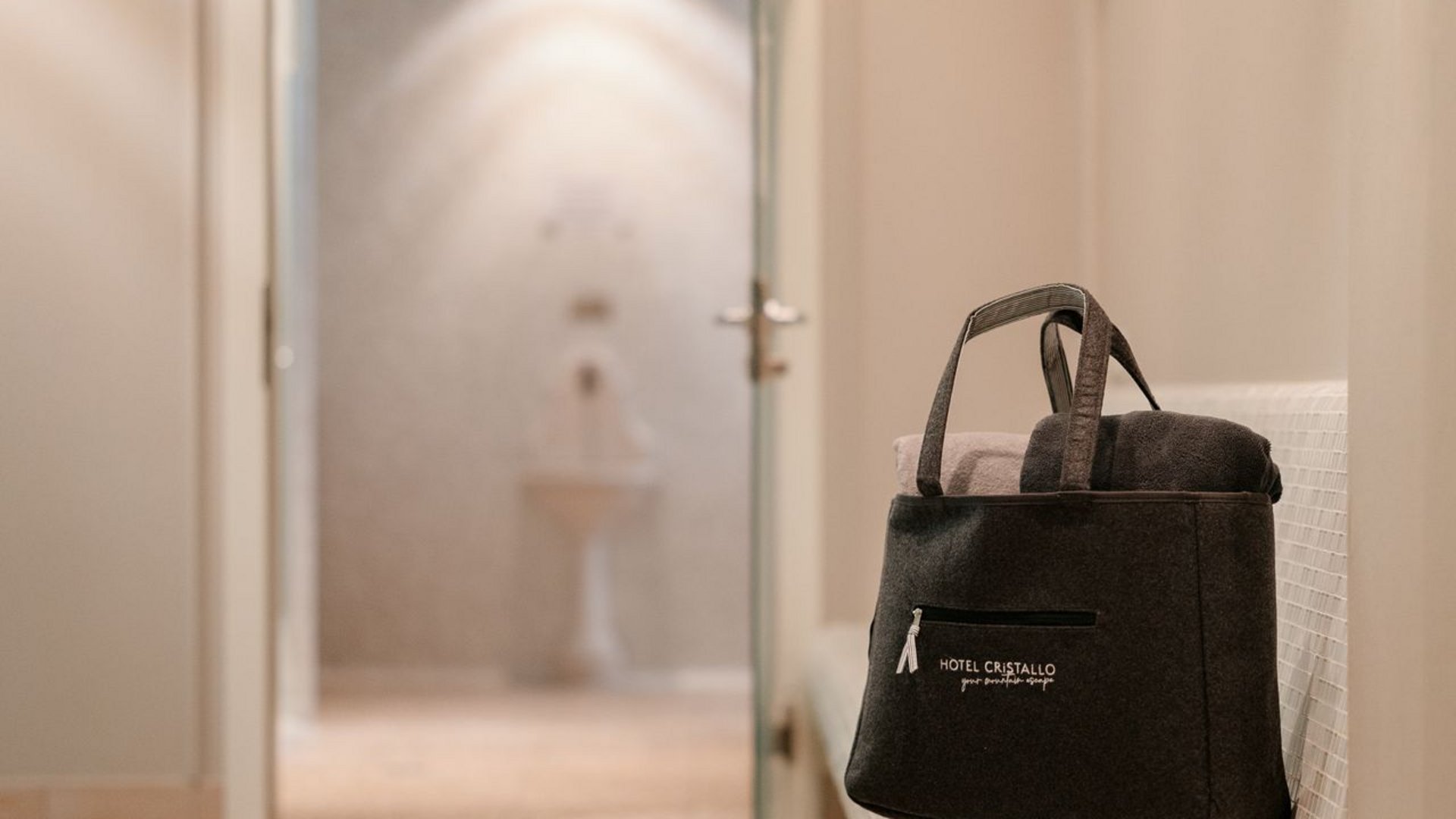 Hotel a Santa Cristina in Val Gardena con piscina: relax puro Area sauna con porta in vetro aperta, borsa sulla panca e ciabatte sul pavimento