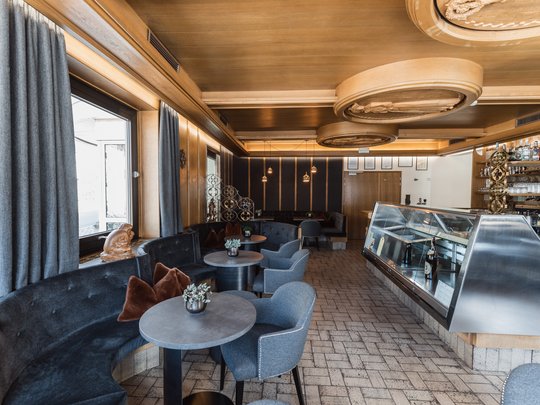 Deine Unterkunft in St. Christina im Grödnertal: Willkommen! Innenaufnahme eines modernen Cafés mit schwarzen Sitzbänken und Theke