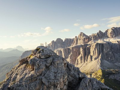 Deine Unterkunft in St. Christina im Grödnertal: Willkommen! Berggipfel mit zwei Personen und einem Gipfelkreuz bei Sonnenlicht