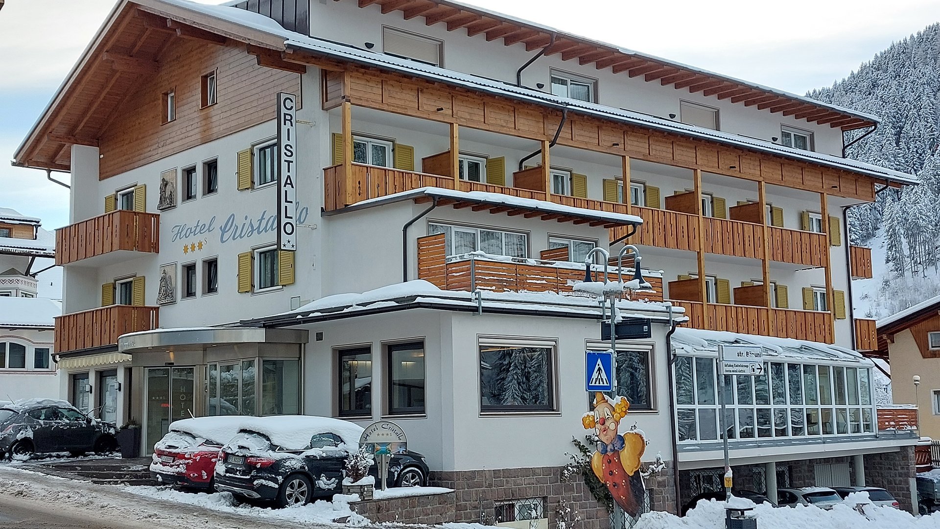 Deine Unterkunft in St. Christina im Grödnertal: Willkommen! Hotel Cristallo im Schnee mit geparkten Autos und verschneiter Landschaft
