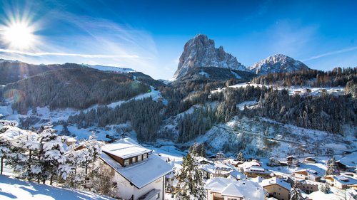 Deine Unterkunft in St. Christina im Grödnertal: Willkommen! Winterlandschaft mit schneebedecktem Dorf und Bergen unter klarem blauem Himmel