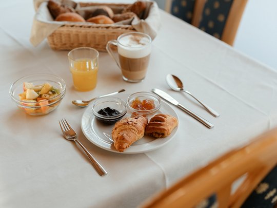 Il nostro hotel a 3 stelle in Val Gardena e la sua cucina Colazione con croissant, marmellata, macedonia e bevande su tavolo bianco