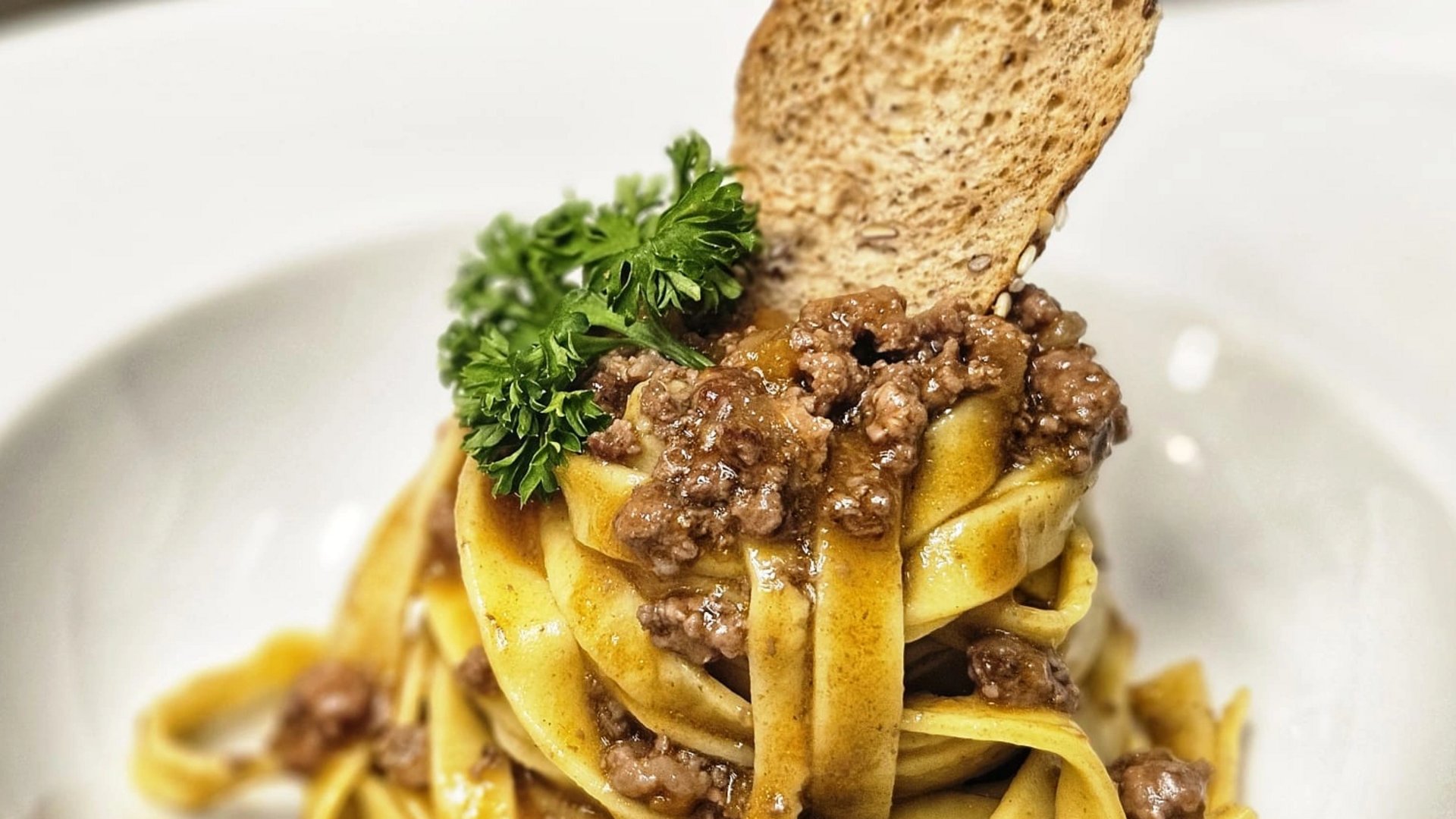 Il nostro hotel a 3 stelle in Val Gardena e la sua cucina Pasta con ragù di carne, prezzemolo e fetta di pane tostato su piatto bianco