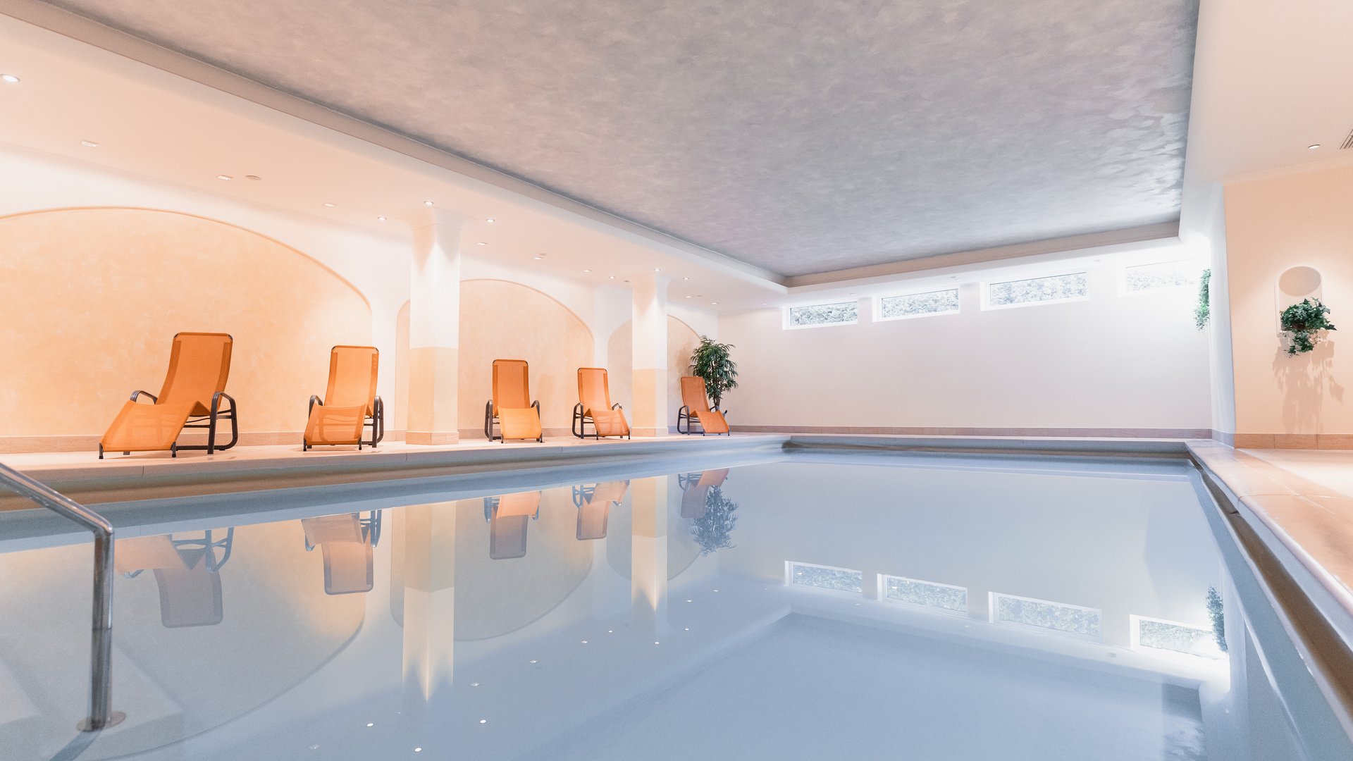 Deine Unterkunft in St. Christina im Grödnertal: Willkommen! Innenpool mit orangen Liegestühlen und hellen Wänden
