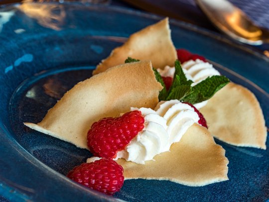 Il nostro hotel a 3 stelle in Val Gardena e la sua cucina Dolce con lamponi, panna montata e biscotti sottili e croccanti su piatto blu