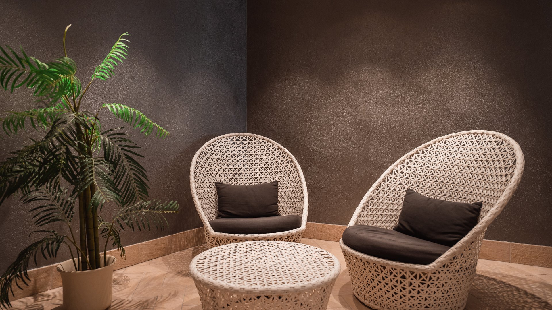 Hotel a Santa Cristina in Val Gardena con piscina: relax puro Set di mobili in rattan bianco con due poltrone e un tavolino in stanza scura