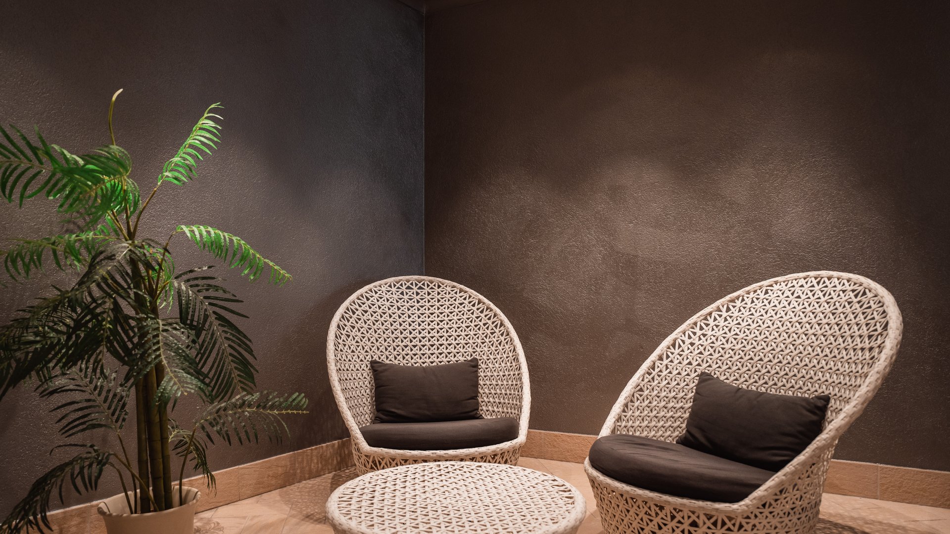 Deine Unterkunft in St. Christina im Grödnertal: Willkommen! Weißes Rattanmöbel-Set mit zwei Sesseln und einem Tisch in dunklem Raum