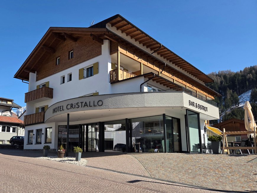 Deine Unterkunft in St. Christina im Grödnertal: Willkommen! Hotel Cristallo mit Bar & Bistrot in einem Dorf mit Bergen im Hintergrund