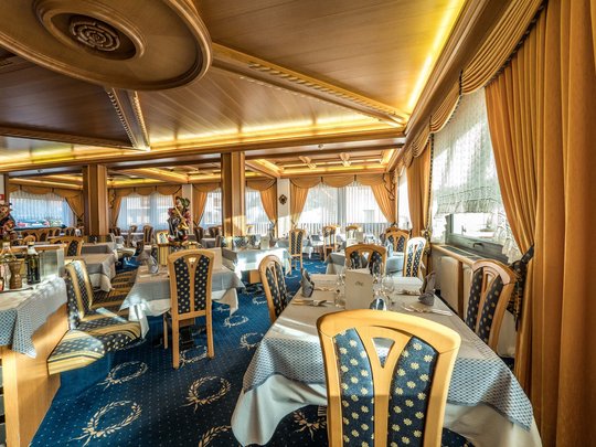Deine Unterkunft in St. Christina im Grödnertal: Willkommen! Elegantes Restaurant mit holzgetäfeltem Decken und blau-gemusterten Stühlen