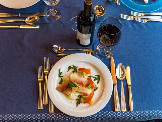 Il nostro hotel a 3 stelle in Val Gardena e la sua cucina Tavola apparecchiata con piatto di pesce, bicchiere di vino rosso e posate su tovaglia blu