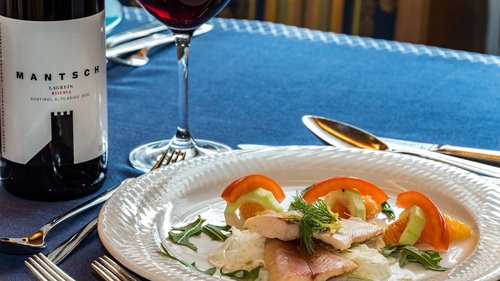 Hotel a 3 stelle a Santa Cristina: per un benessere stellare Piatto con filetto di pesce, verdure e fette d'arancia su piatto bianco, bicchiere di vino rosso vicino