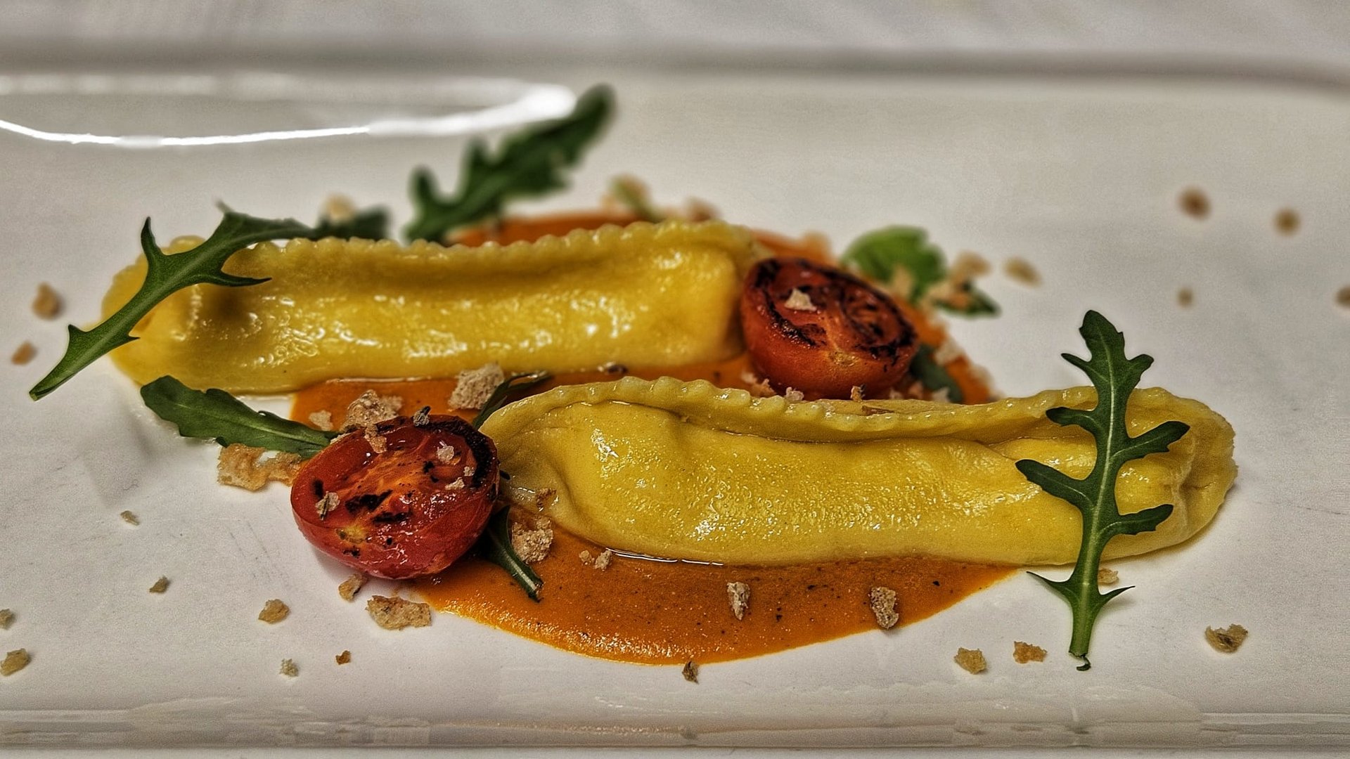 Il nostro hotel a 3 stelle in Val Gardena e la sua cucina Due ravioli su salsa con pomodoro grigliato e rucola su piatto bianco